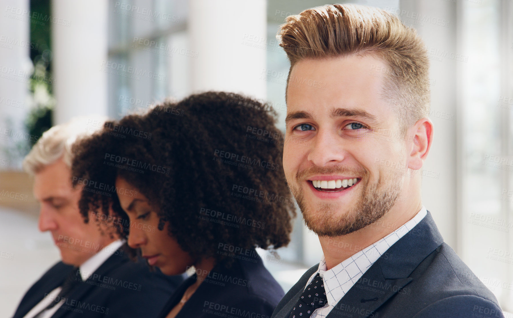 Buy stock photo Cropped portrait of a handsome young businessman smiling while sitting in a line with his colleagues in the office