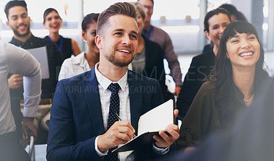 Buy stock photo Cropped shot of a handsome young businessman sitting with his colleagues and holding a notebook while in the office