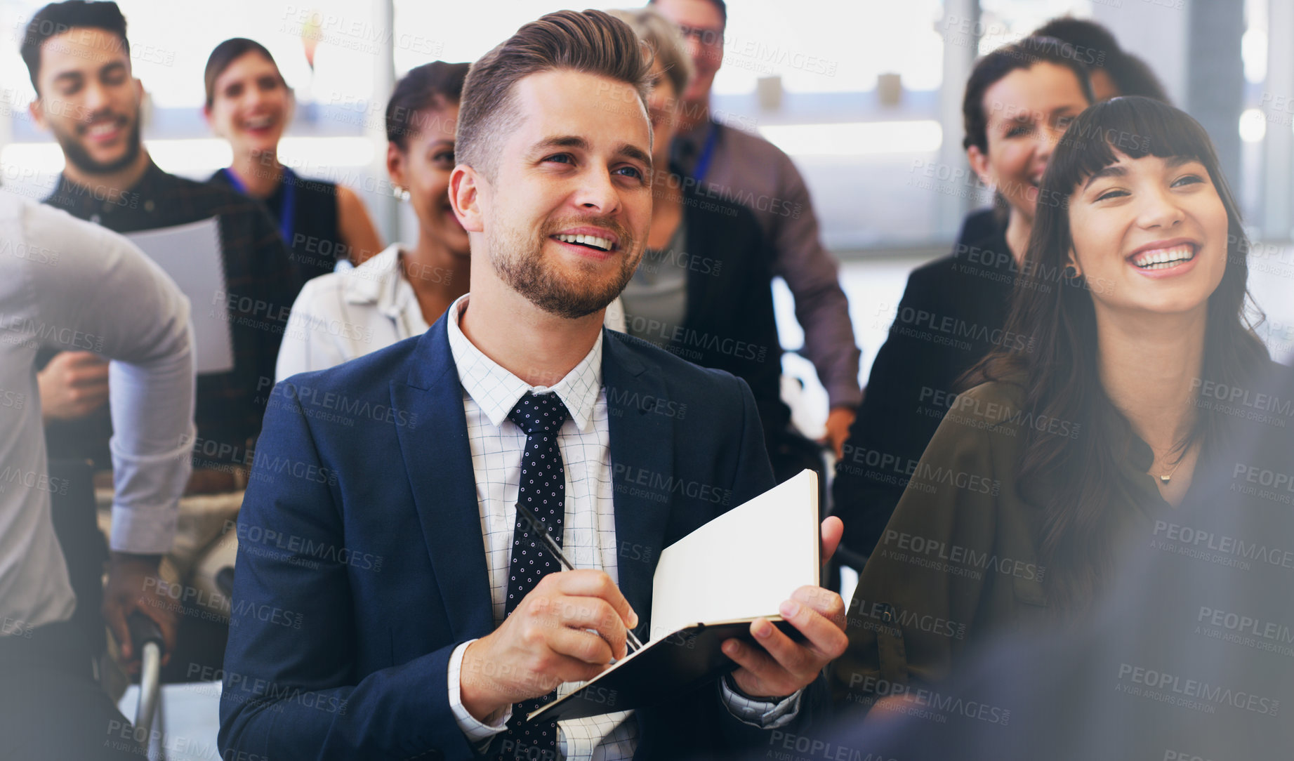 Buy stock photo Cropped shot of a handsome young businessman sitting with his colleagues and holding a notebook while in the office