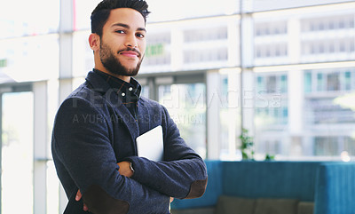 Buy stock photo Cropped portrait of a handsome young businessman standing with his arms folded ad holding a tablet while in the office