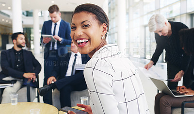 Buy stock photo Cropped portrait of an attractive young businesswoman sitting and smiling while her colleagues work behind her in the office
