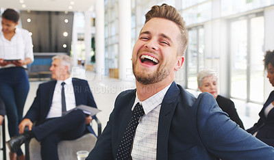 Buy stock photo Cropped portrait of a handsome young businessman sitting and laughing while his colleagues work behind him in the office