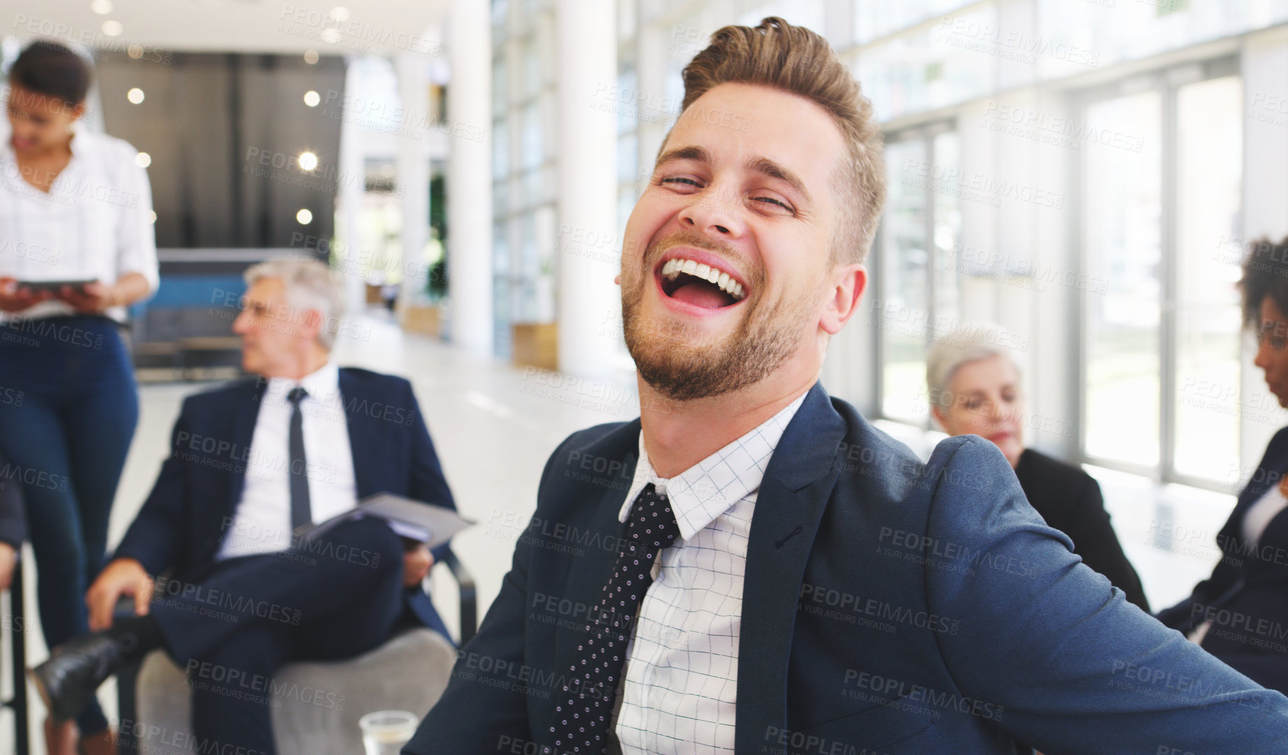 Buy stock photo Cropped portrait of a handsome young businessman sitting and laughing while his colleagues work behind him in the office