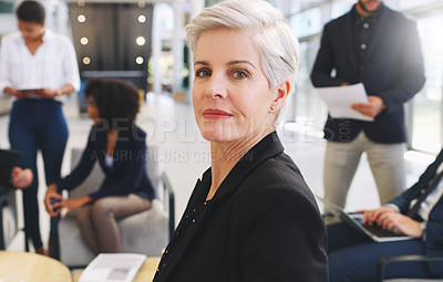 Buy stock photo Cropped portrait of an attractive mature businesswoman sitting while her colleagues work behind her in the office