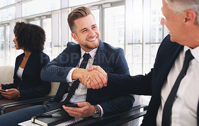 Buy stock photo Cropped shot of a handsome young businessman shaking hands with a colleague while sitting in a line in the office