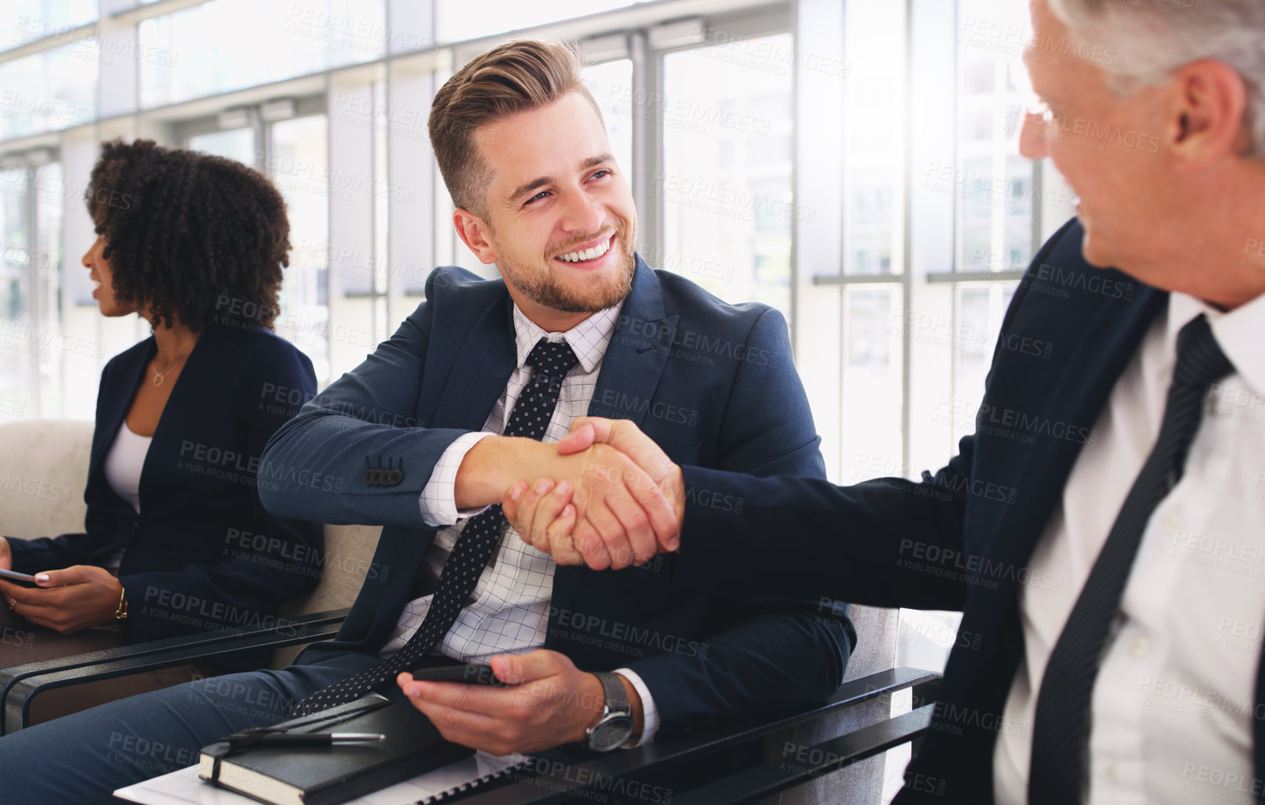 Buy stock photo Cropped shot of a handsome young businessman shaking hands with a colleague while sitting in a line in the office