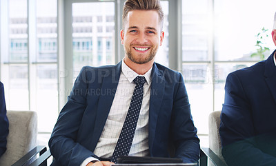 Buy stock photo Cropped portrait of a handsome young businessman sitting and smiling while in the office during the day