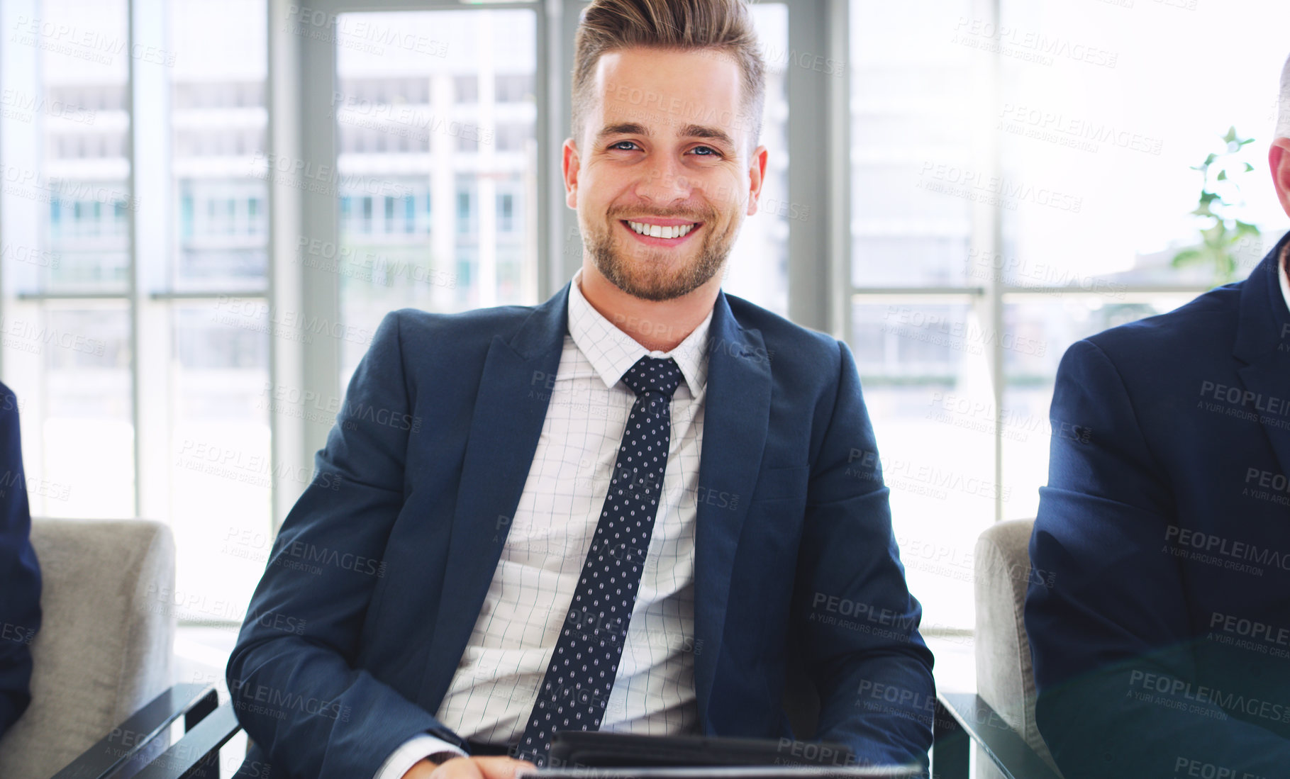 Buy stock photo Cropped portrait of a handsome young businessman sitting and smiling while in the office during the day