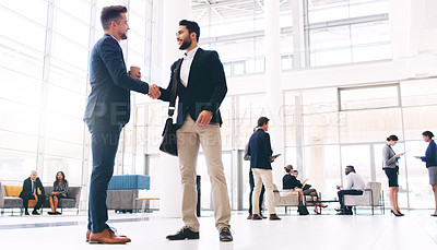 Buy stock photo Full length shot of two handsome young businessmen shaking hands while their colleagues work behind them in the office