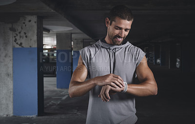 Buy stock photo Shot of a handsome young sportsman checking his watch while exercising inside a parking lot