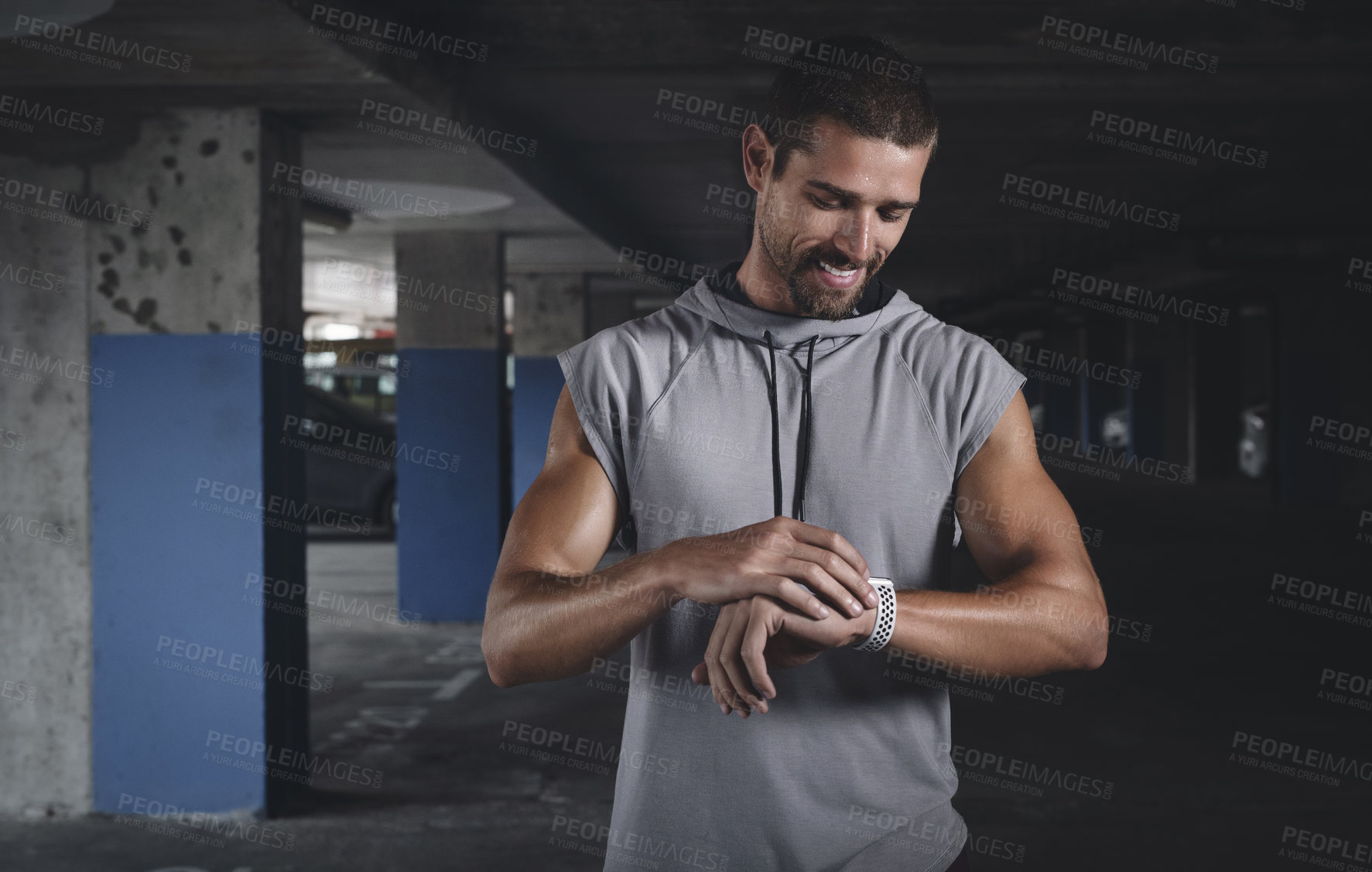 Buy stock photo Shot of a handsome young sportsman checking his watch while exercising inside a parking lot