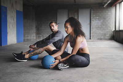 Buy stock photo Full length shot of sporty young couple sitting down and exercising with a ball inside a parking lot