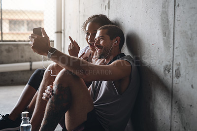 Buy stock photo Shot of a sporty young couple using a cellphone together while  sitting down and resting against a wall