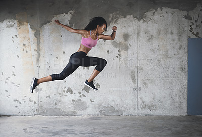 Buy stock photo Full length shot of an athletic young sportswoman jumping in the air against a wall outdoors
