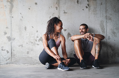 Buy stock photo Full length shot of a sporty young couple sitting down and resting against a wall while exercising outdoors