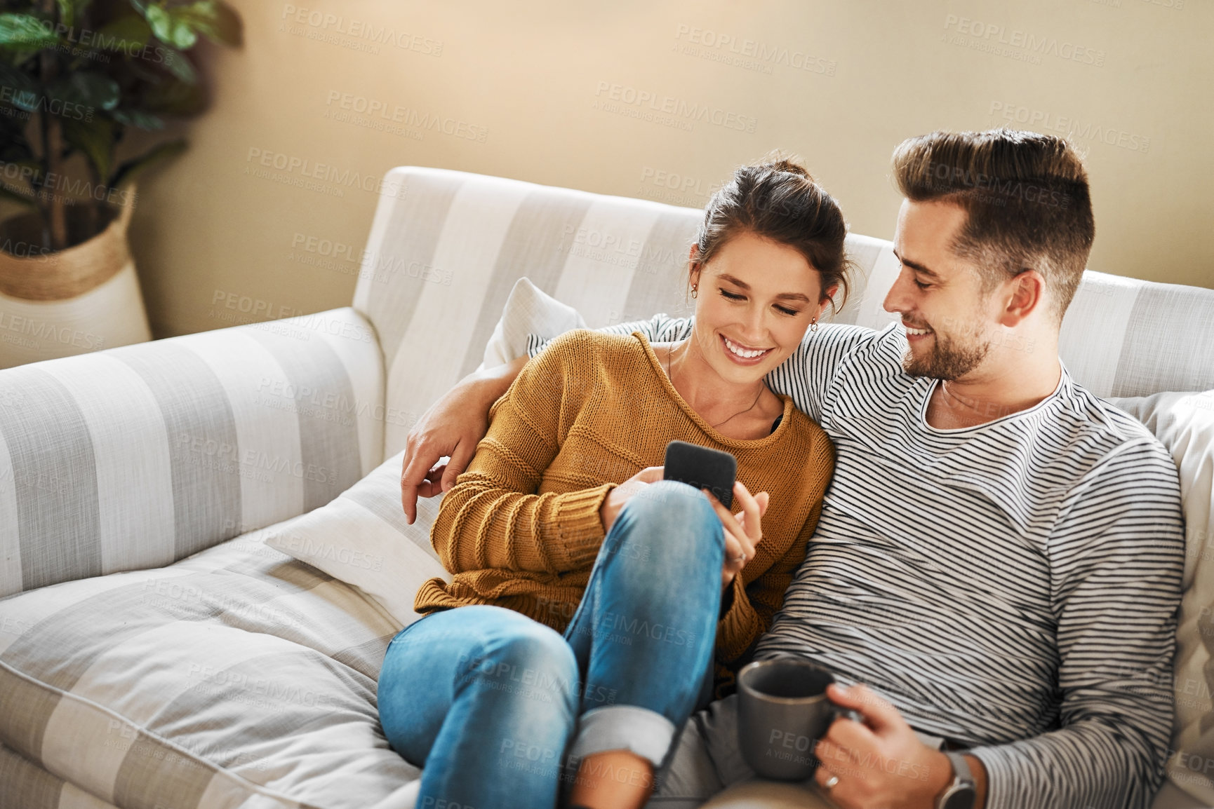 Buy stock photo Shot of a young couple using a cellphone while relaxing on the sofa at home