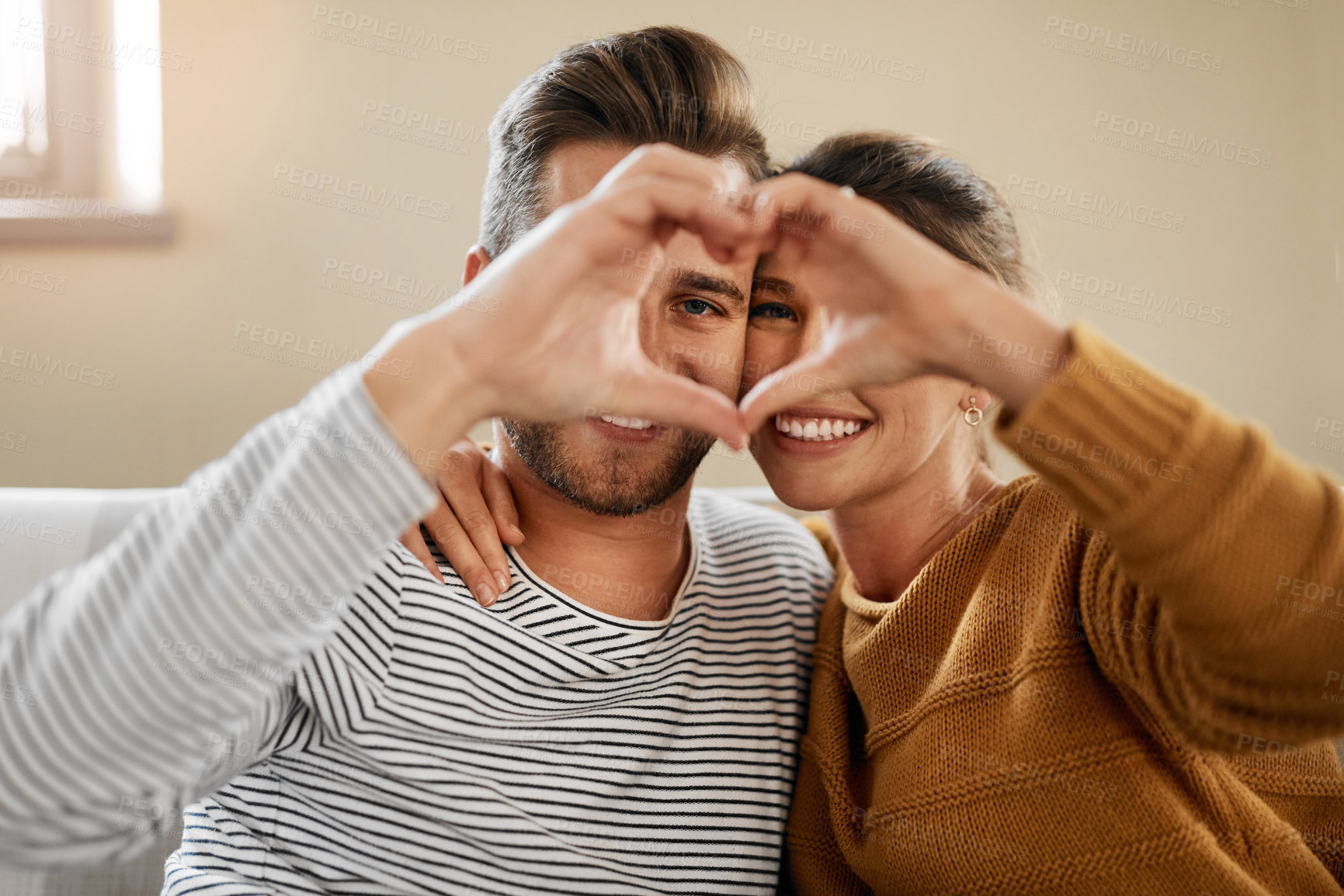 Buy stock photo Shot of a couple forming a heart shape with their hands while sitting together