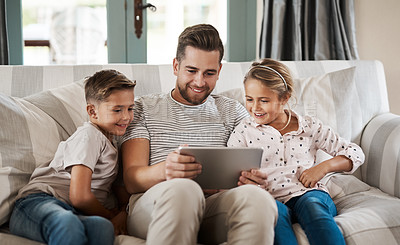 Buy stock photo Shot of an adorable little girl and boy using a digital tablet with their father on the sofa at home