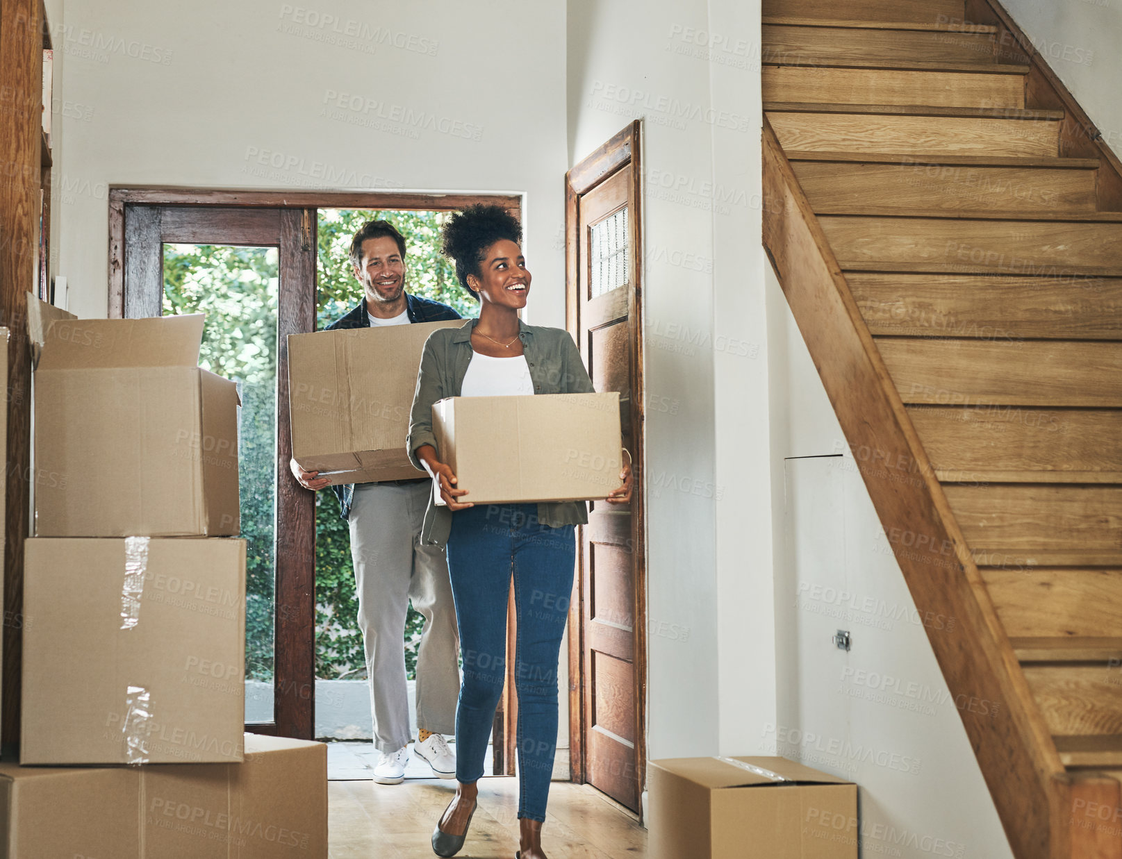 Buy stock photo Interracial couple moving into a new modern house, carrying boxes and arriving home together. Happy, excited and smiling husband and wife walking, entering and relocating after buying an apartment