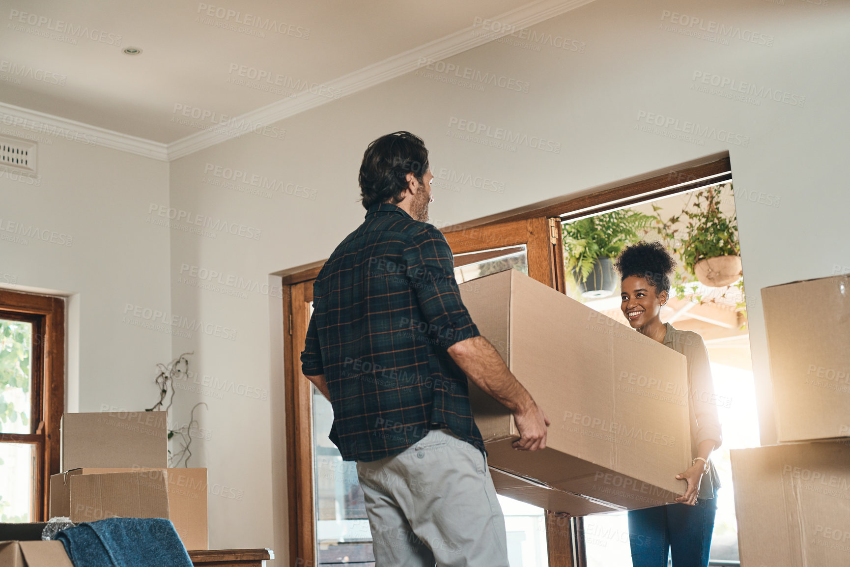 Buy stock photo Cropped shot of an affectionate young couple assisting each other to carry a box into their new home