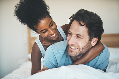 Buy stock photo Interracial, playful and loving couple cuddling in bed and enjoying the weekend together at home. Affectionate, happy and bonding diverse lovers embracing and having fun in their bedroom