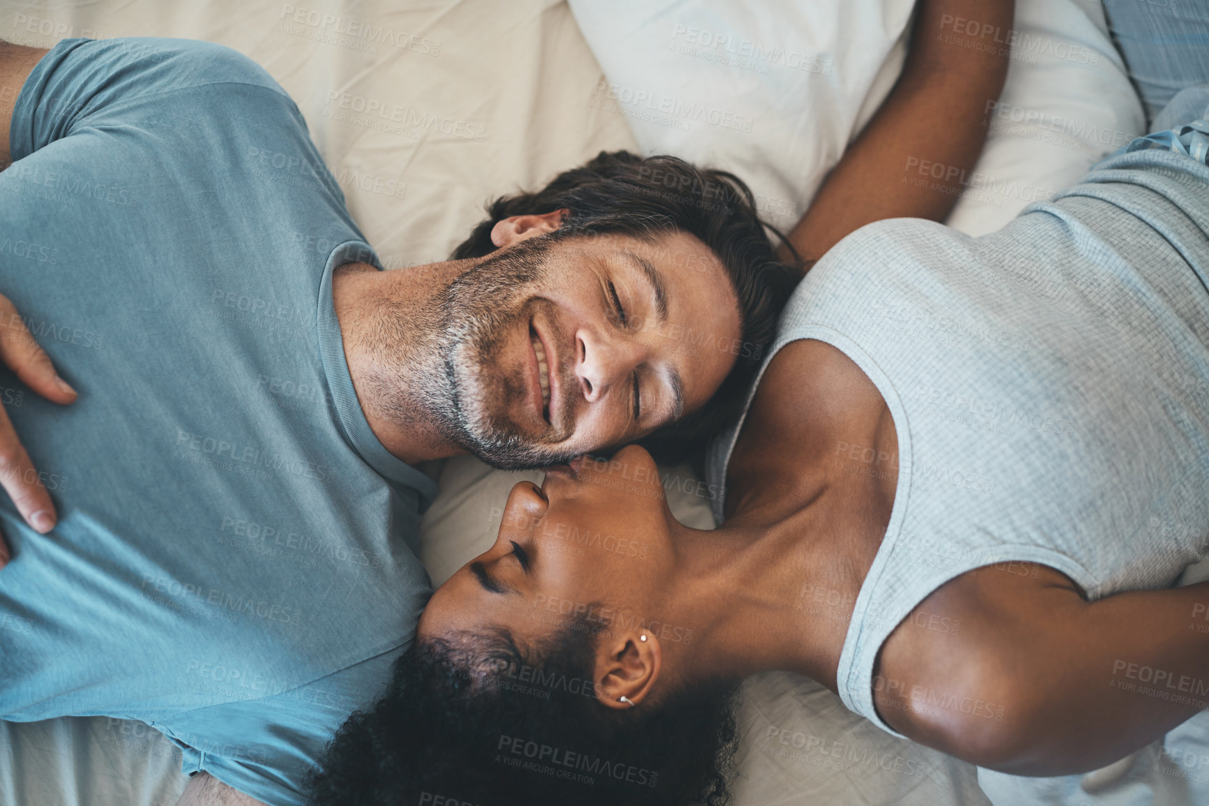 Buy stock photo Interracial couple, kiss and relax on bed above for morning bonding, intimate relationship or love at home. Top view of woman kissing man while lying in bedroom for loving romance, care or affection