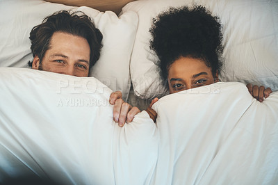 Buy stock photo Top view of a romantic young couple in love having fun covering with a blanket and bonding. A cute interracial husband and wife relationship peeking over sheets on an intimate honeymoon 