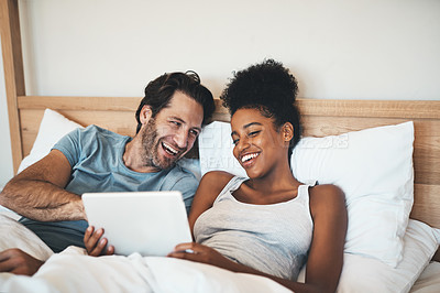 Buy stock photo Happy, relaxed and carefree couple reading social media news on digital tablet and laughing in bed. Interracial husband and wife waking up together and browsing internet, sharing a funny online joke