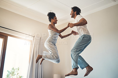 Buy stock photo Full length shot of an affectionate young couple jumping playfully on their bed at home