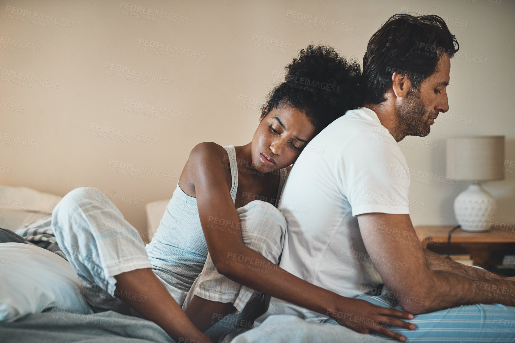 Buy stock photo Woman tries to embrace her husband with affection after their fight at home. Unhappy interracial couple with marriage problems forgive each other. Empathy and guilty feelings after the affair.