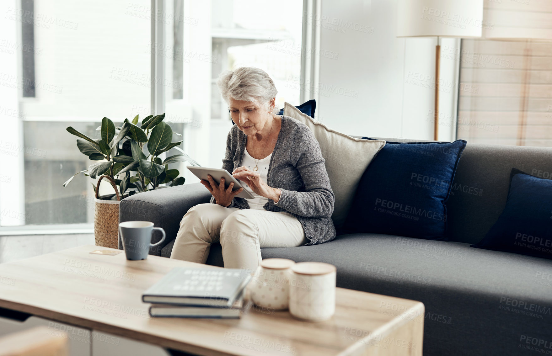 Buy stock photo Shot of a senior woman using a digital tablet while relaxing at home