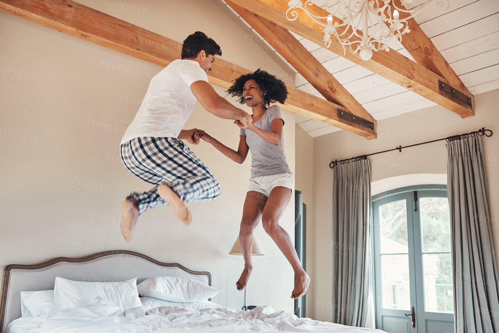 Buy stock photo Full length sho of a playful young couple jumping on bed together at home
