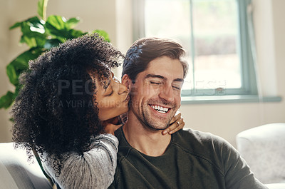 Buy stock photo Shot of a young woman kissing her boyfriend on the cheek while spending some quality time together at home