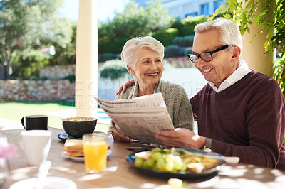 Buy stock photo Shot of an affectionate senior couple reading the newspaper while enjoying a meal together outdoors
