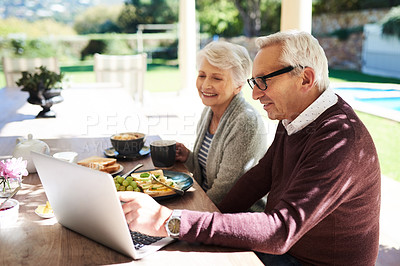 Buy stock photo Shot of an affectionate senior couple using a laptop while enjoying a meal together outdoors