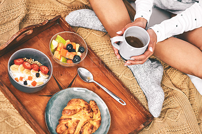 Buy stock photo Aerial shot of an unrecognizable woman holding a cup of coffee while sitting with an arranged breakfast tray in bed