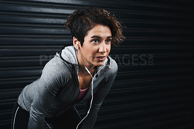 Buy stock photo Cropped shot of an attractive young woman wearing earphones and taking a break against a black background after exercising