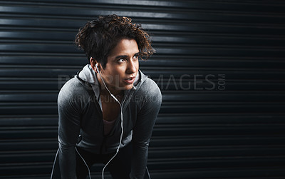 Buy stock photo Cropped shot of an attractive young woman wearing earphones and taking a break against a black background after exercising