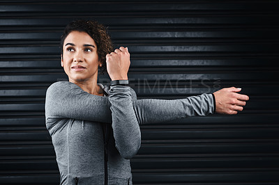 Buy stock photo Cropped shot of an attractive young woman standing against a black background and stretching after her workout