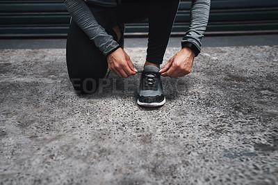 Buy stock photo Cropped shot of an unrecognizable woman crouched down and tying her shoes before running outside