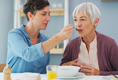 Buy stock photo Cropped shot of an attractive young woman helping and feeding her senior mother while they have breakfast together at home