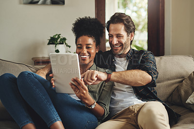 Buy stock photo Shot of a happy young couple using a digital tablet together while relaxing on a couch at home