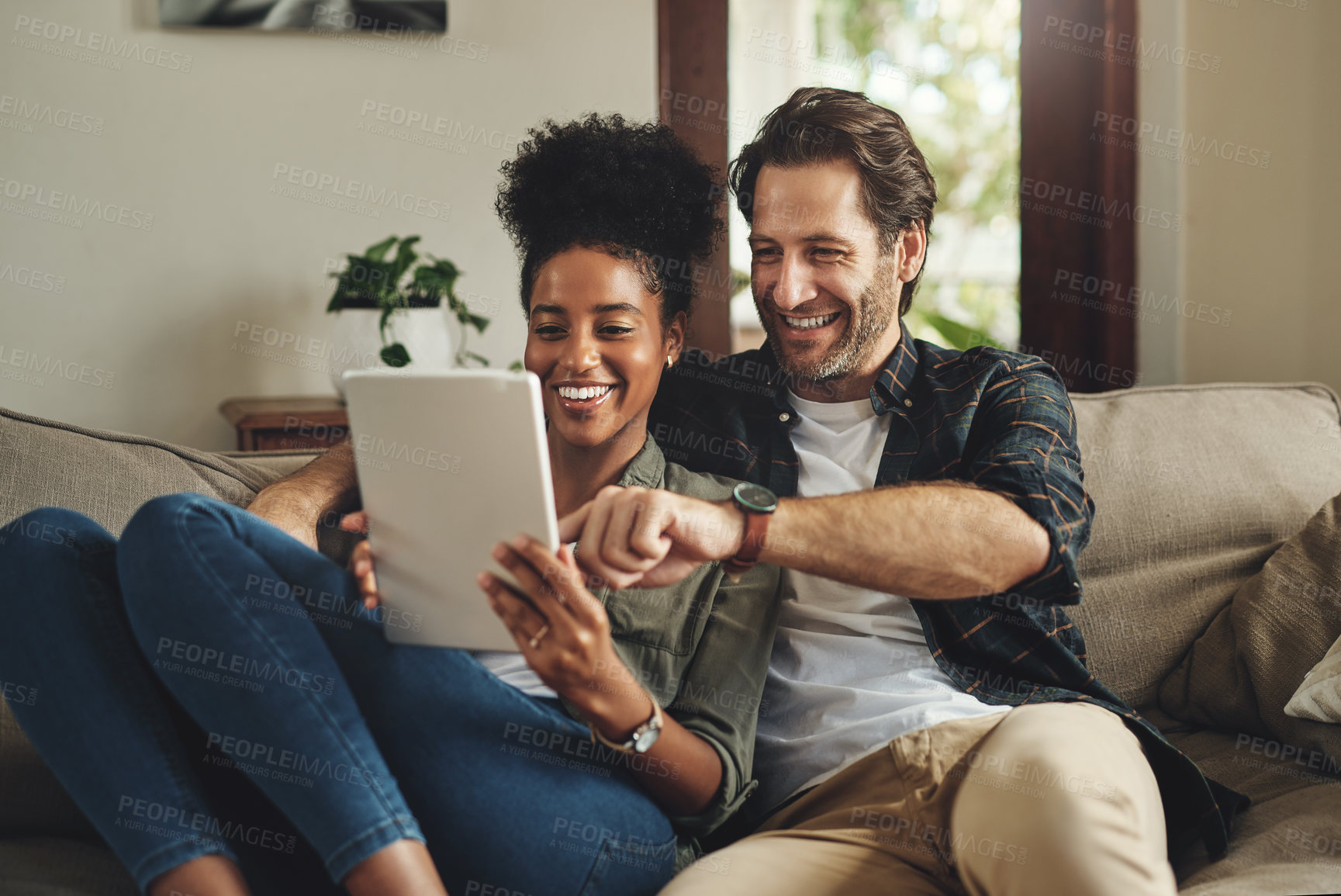 Buy stock photo Shot of a happy young couple using a digital tablet together while relaxing on a couch at home