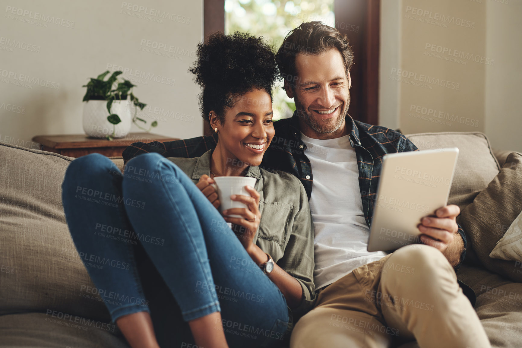 Buy stock photo Relax, home and interracial couple on a couch, tablet and happiness with social media and connection. Partners, man and woman on a sofa, technology and loving with a smile, romance and online reading