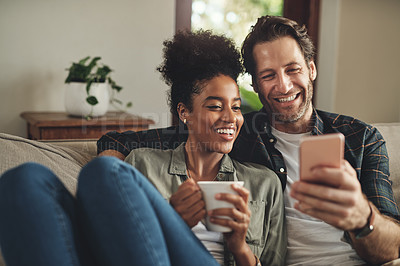 Buy stock photo Shot of a happy young couple using a cellphone together while relaxing on a couch at home