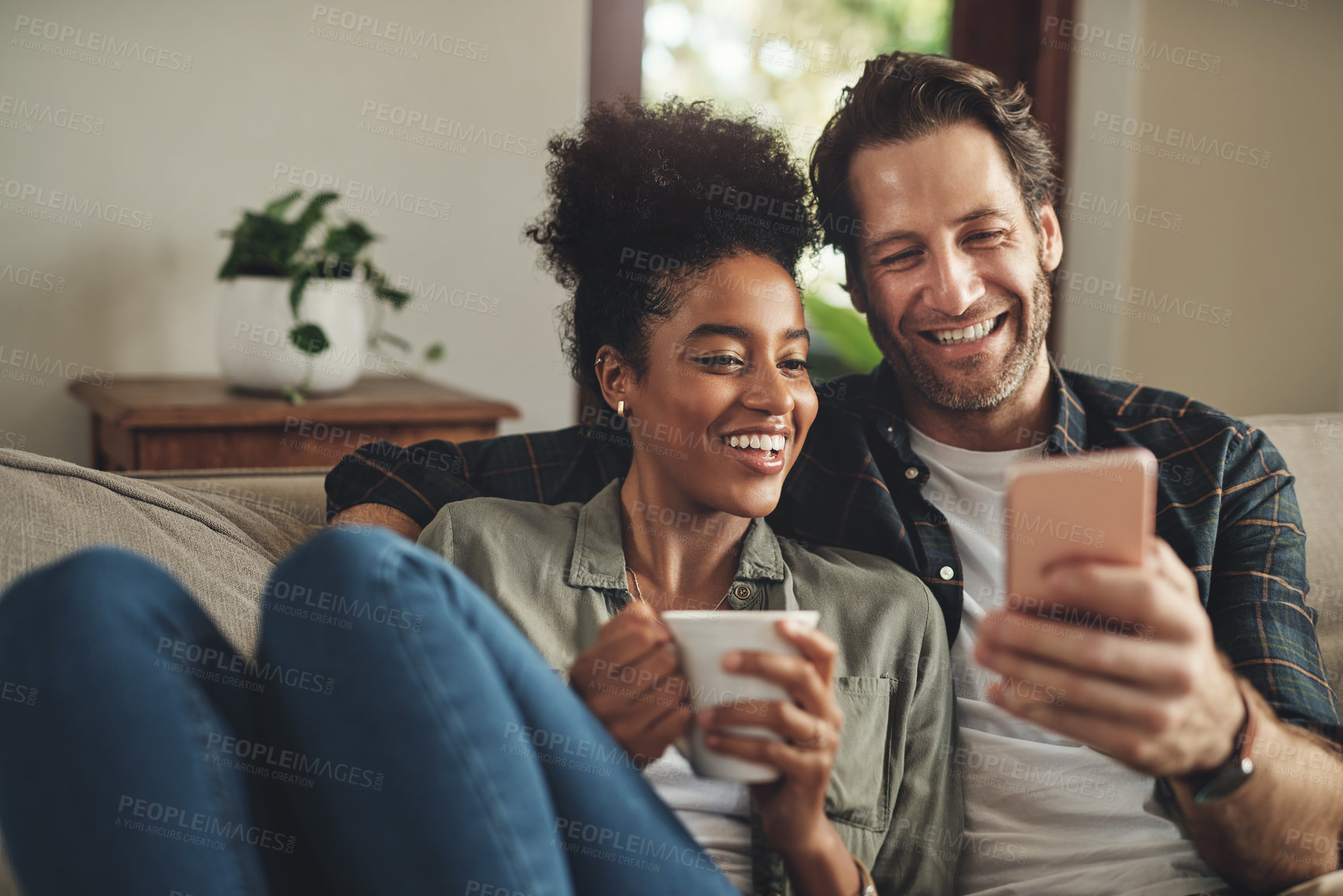 Buy stock photo Shot of a happy young couple using a cellphone together while relaxing on a couch at home