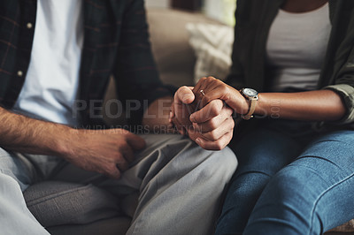 Buy stock photo Shot of an unrecognizable couple holding hands while sitting on a sofa at home