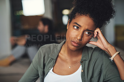 Buy stock photo Shot of an attractive young woman looking upset while her boyfriend sits in the background at home