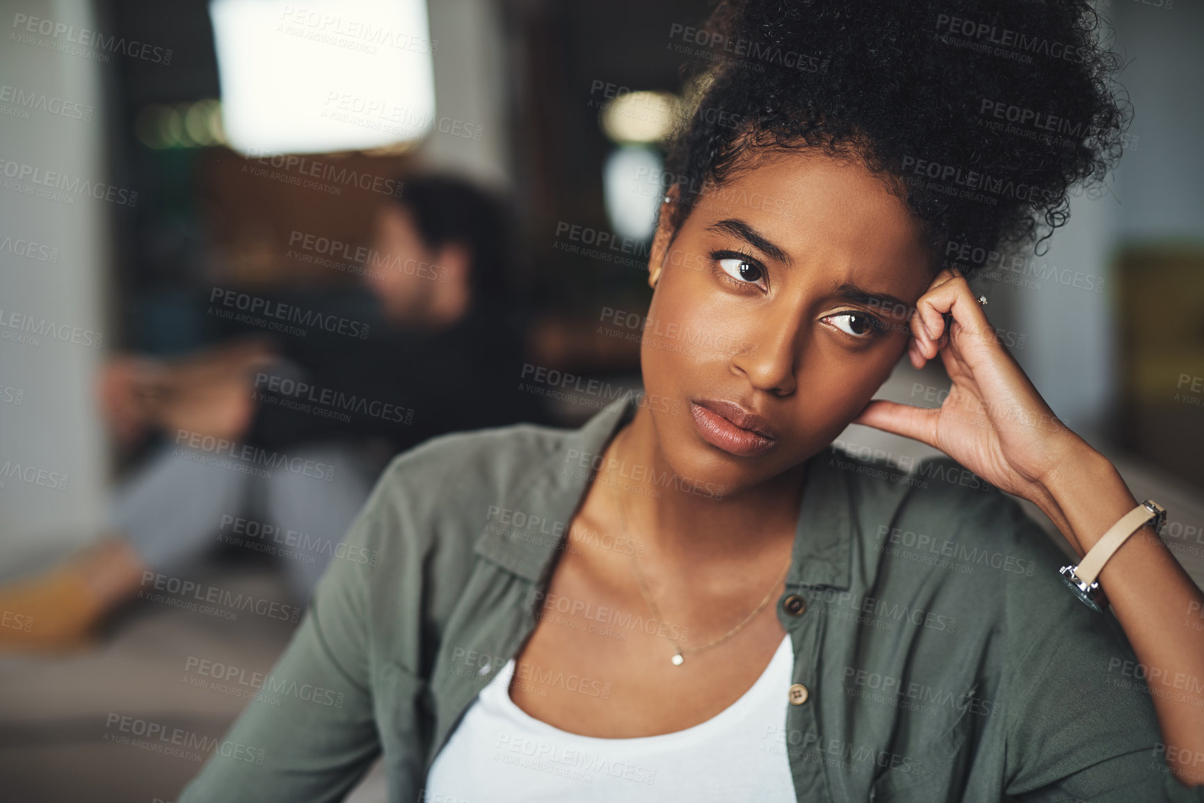 Buy stock photo Shot of an attractive young woman looking upset while her boyfriend sits in the background at home