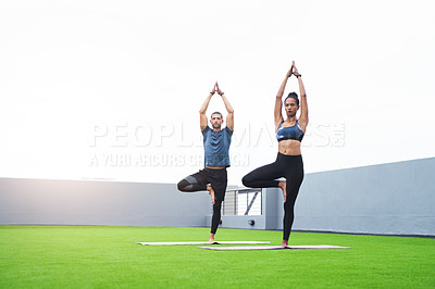 Buy stock photo Shot of a young man and woman practising yoga together outdoors